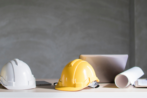 A desk with a two builders hats and a laptop